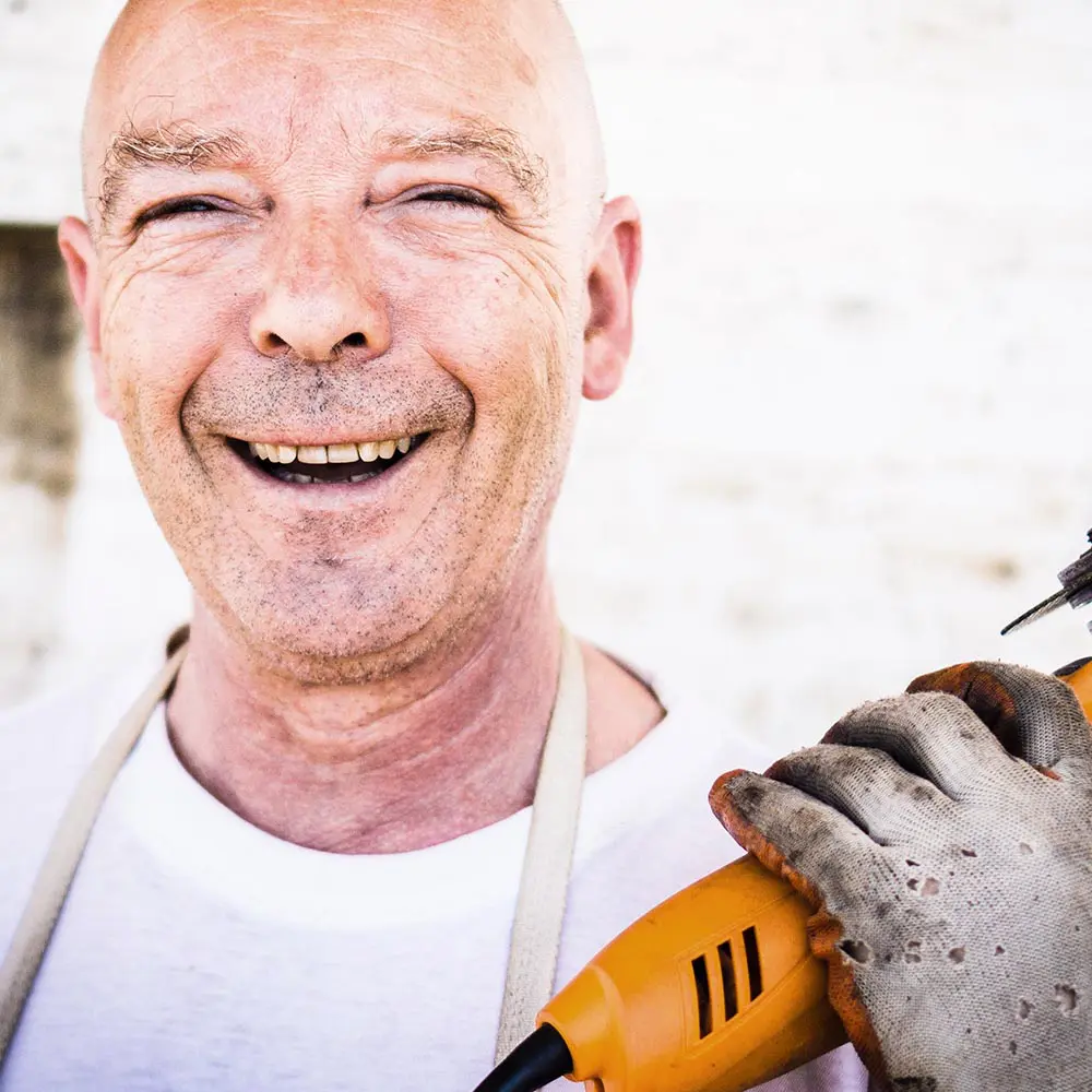 Lachender Handwerker mit einem Werkzeug in der Hand.