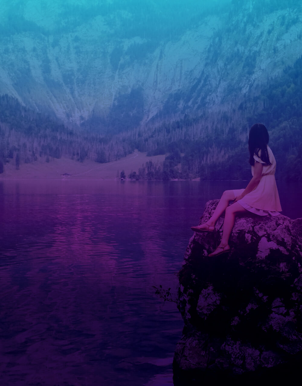 Junge Frau sitzt auf einem Stein am Wasser und schaut auf die Berge.