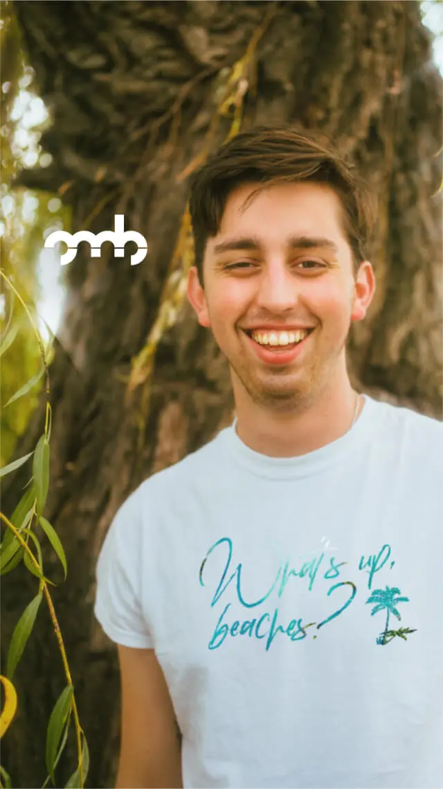 Mann mit mit einem Short von Oh, my Brand! mit What's up beaches? Design steht vor einem Baum.