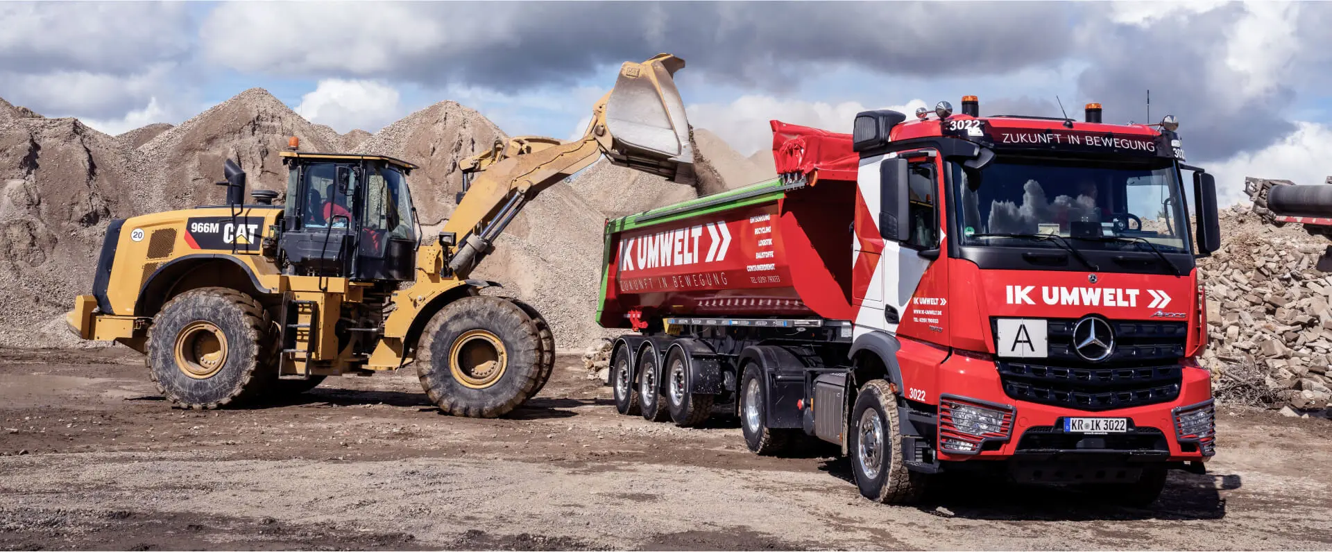 Bagger belädt einen IK Umwelt LKW mit Sand und Erde.