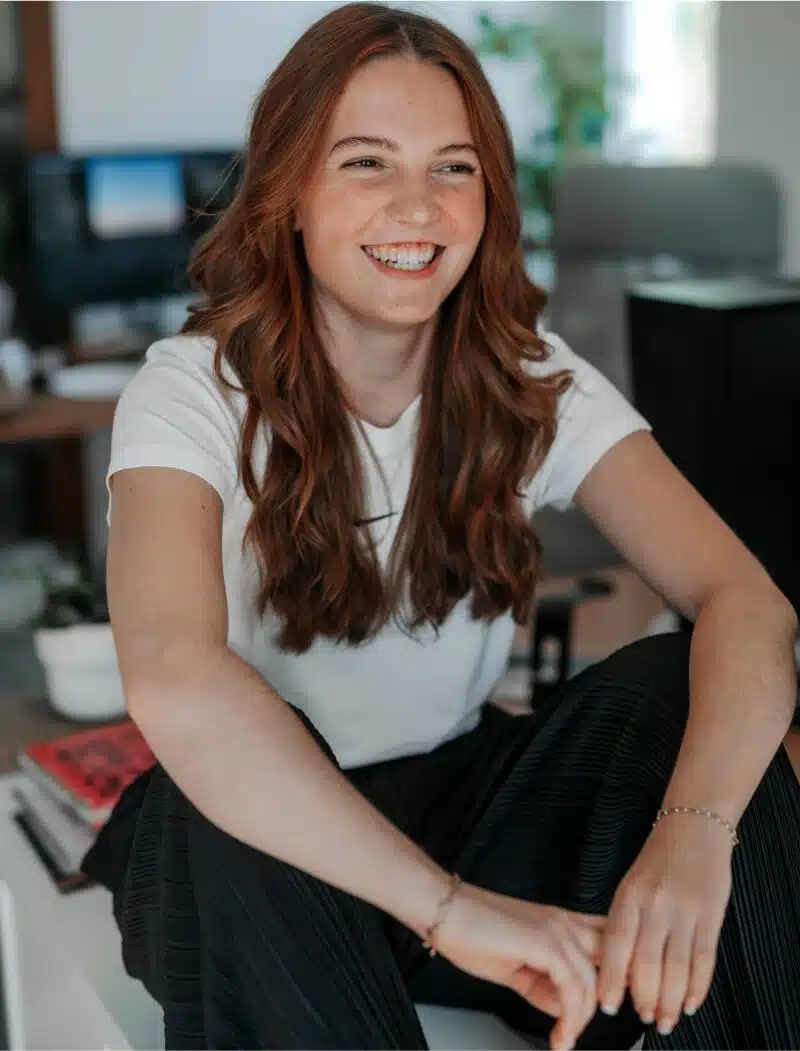 Portrait von Annalena die auf einem Tisch sitzt und lacht.
