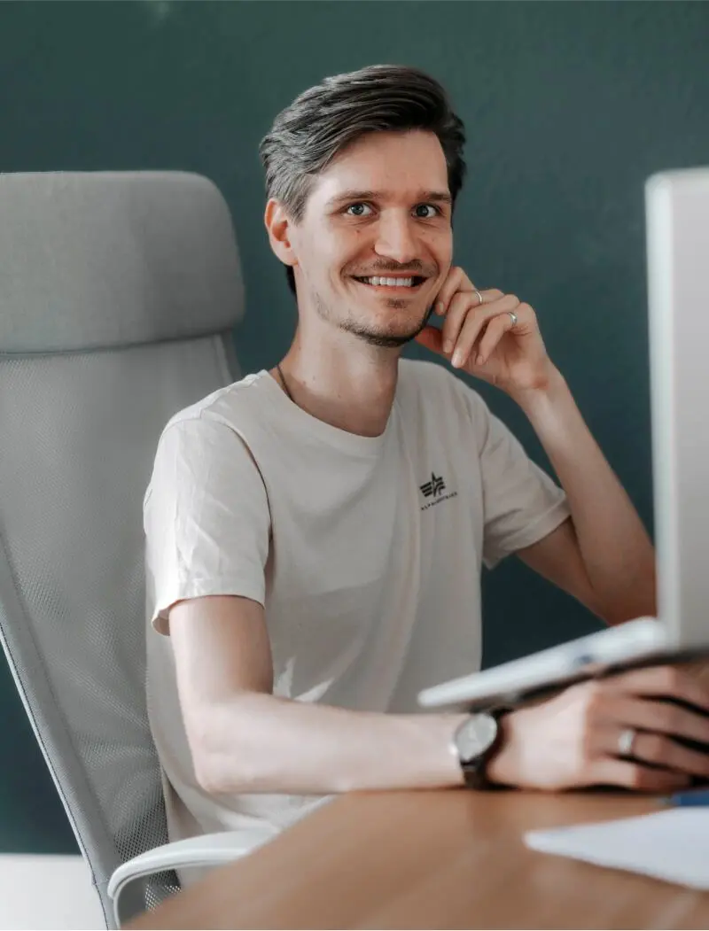 Portrait von Calvin, der an seinem Arbeitsplatz vor dem Bildschirm sitzt und in die Kamera lacht.