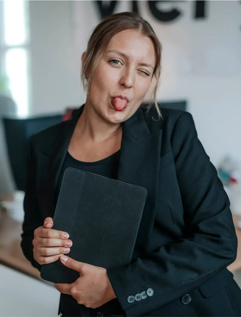 Portrait von Jasmin, die vor ihrem Arbeitsplatz steht und ironisch die Zunge rausstreckt.