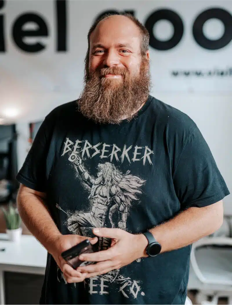 Portrait von Oli, der mit seinem wuschigen Bart in die Kamera lacht.