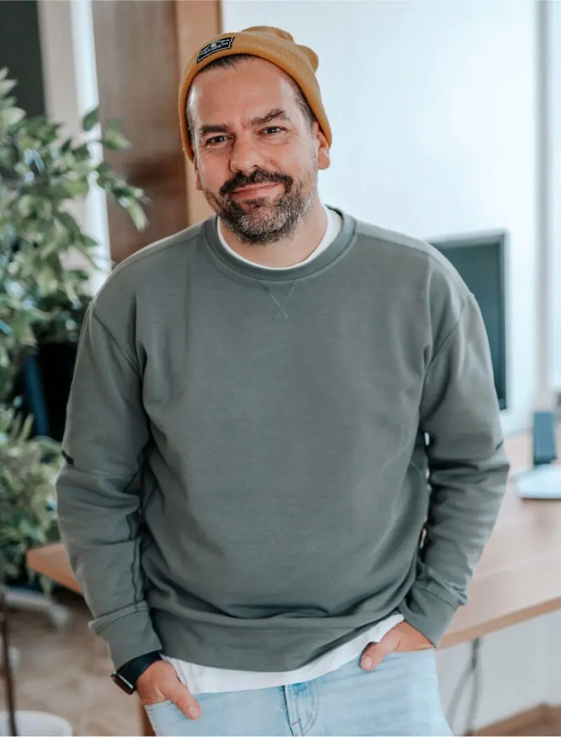Portrait von Tim mit gelbem Beanie, der in die Kamera lacht.