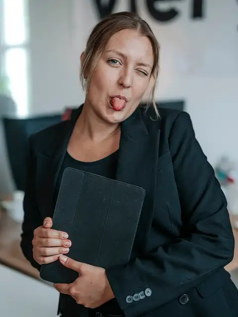 Portrait von Jasmin, die vor ihrem Arbeitsplatz steht und ironisch die Zunge rausstreckt.